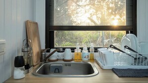 Une cuisine équipée d’un évier, d’une planche à découper en bois, d’une bouilloire en acier inoxydable et d’un égouttoir à vaisselle.
