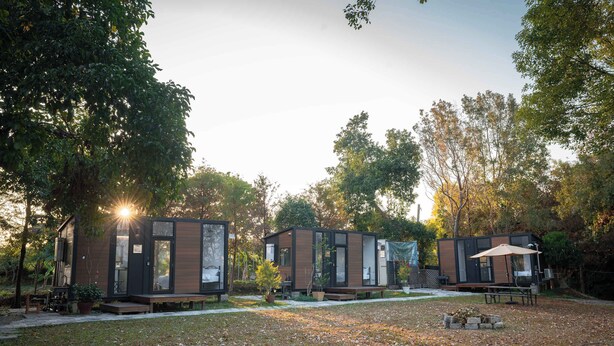 Une rangée de cabines modernes et compactes, dotées de grandes fenêtres, entourée d’une zone herbeuse et d’arbres.