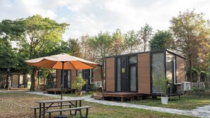Un espace extérieur moderne, doté d’une table de pique-nique et d’un parasol, entouré de cabanes en bois et d’arbres.