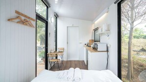 Ein modernes Schlafzimmer mit Bett, einer Holzgalerie für Kleiderbügel, einem Schreibtisch mit Stühlen und Blick ins Freie.
