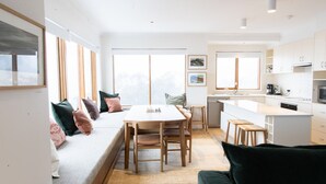 A modern kitchen with white cabinets, a dining area with a wooden table and chairs, and a built-in bench with cushions.
