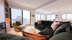 A spacious living room with a large window, a sofa set, and a kitchen area.