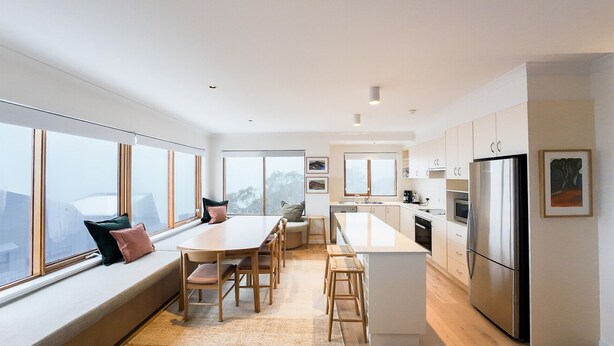 A modern kitchen with a central island, large windows, and a seating area by the window.