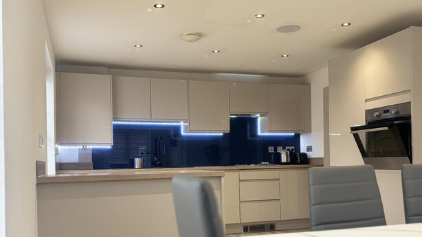 A modern kitchen with a dark backsplash, recessed ceiling lights, and a built-in oven. - Immaculate 4-bed House in Horley (Horley)