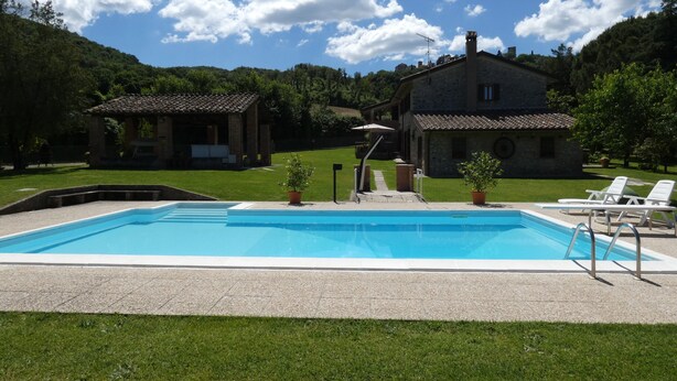 A swimming pool with a stone deck, surrounded by a grassy area and two buildings. - SCAPPO IN UMBRIA, The Piccino (Amelia)
