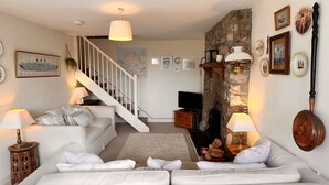 A living room with a white sofa, a wooden coffee table, a TV, and a stone fireplace. - Charming 3 Bedroom Family Cottage - Dogs Welcome (Beaumaris)