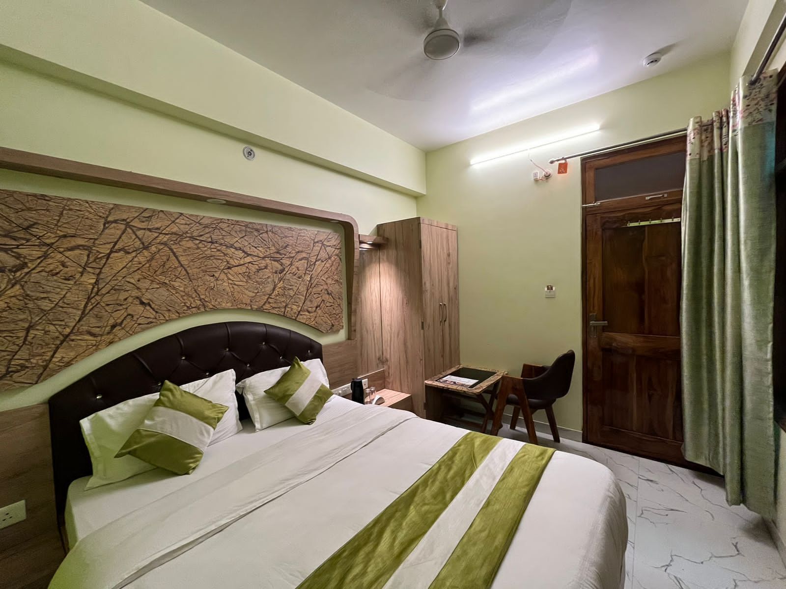 Habitación de hotel con cama, armario de madera, escritorio y silla, y puerta con cortinas.