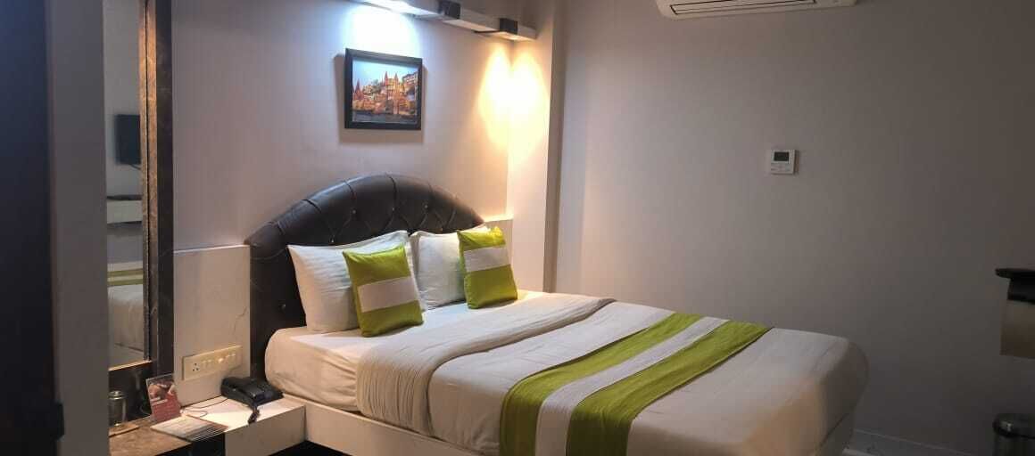 A neatly made bed with a headboard, a bedside table with a lamp, and a wall-mounted picture.