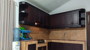 A kitchen with dark wooden cabinets, a tiled backsplash, and a water dispenser on a stool. - Hotel O Karunia Kost & PenginapanNearSiring Marabahan (Ulek Barito) (Marabahan)