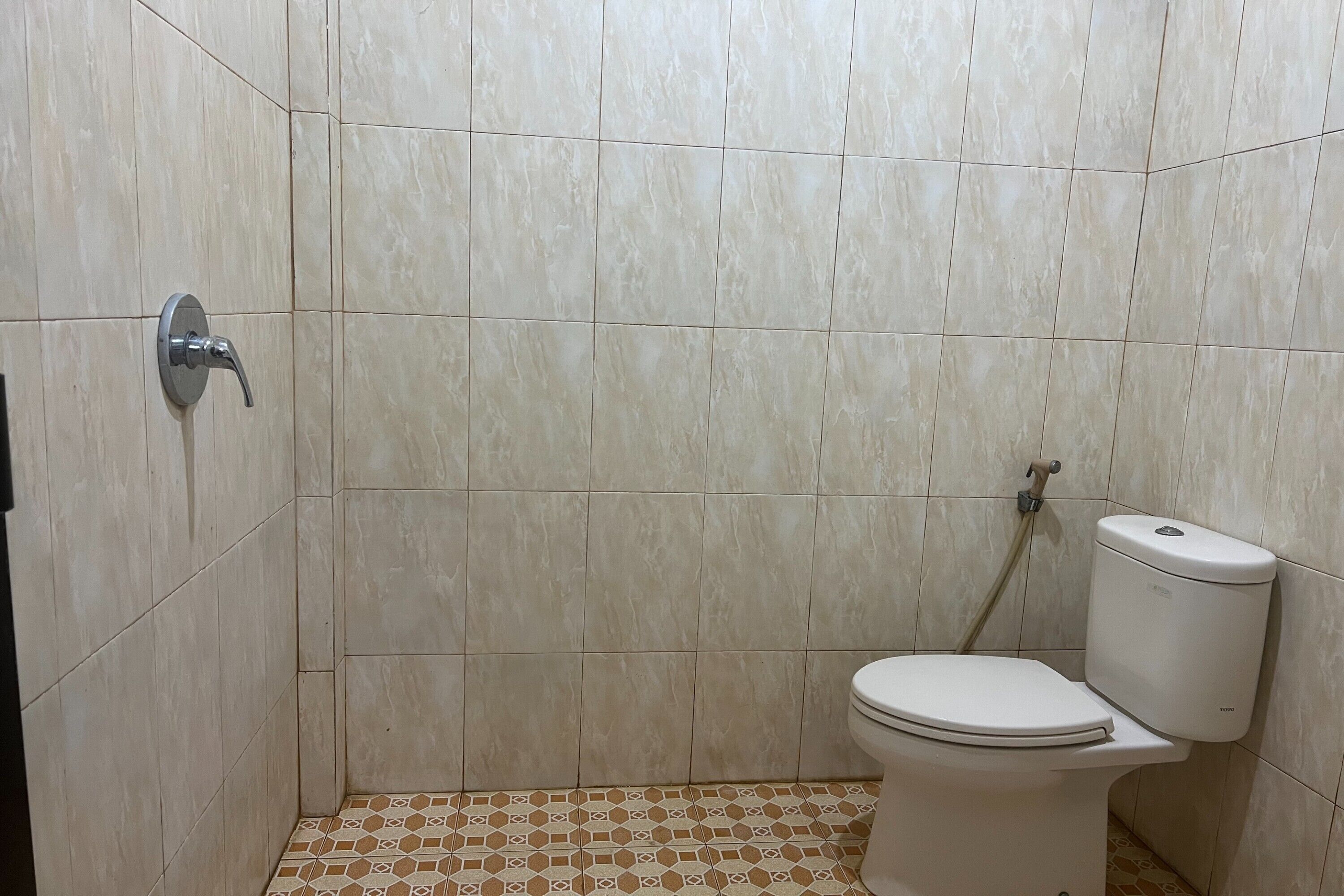 Un baño con inodoro, ducha y suelo de baldosas.