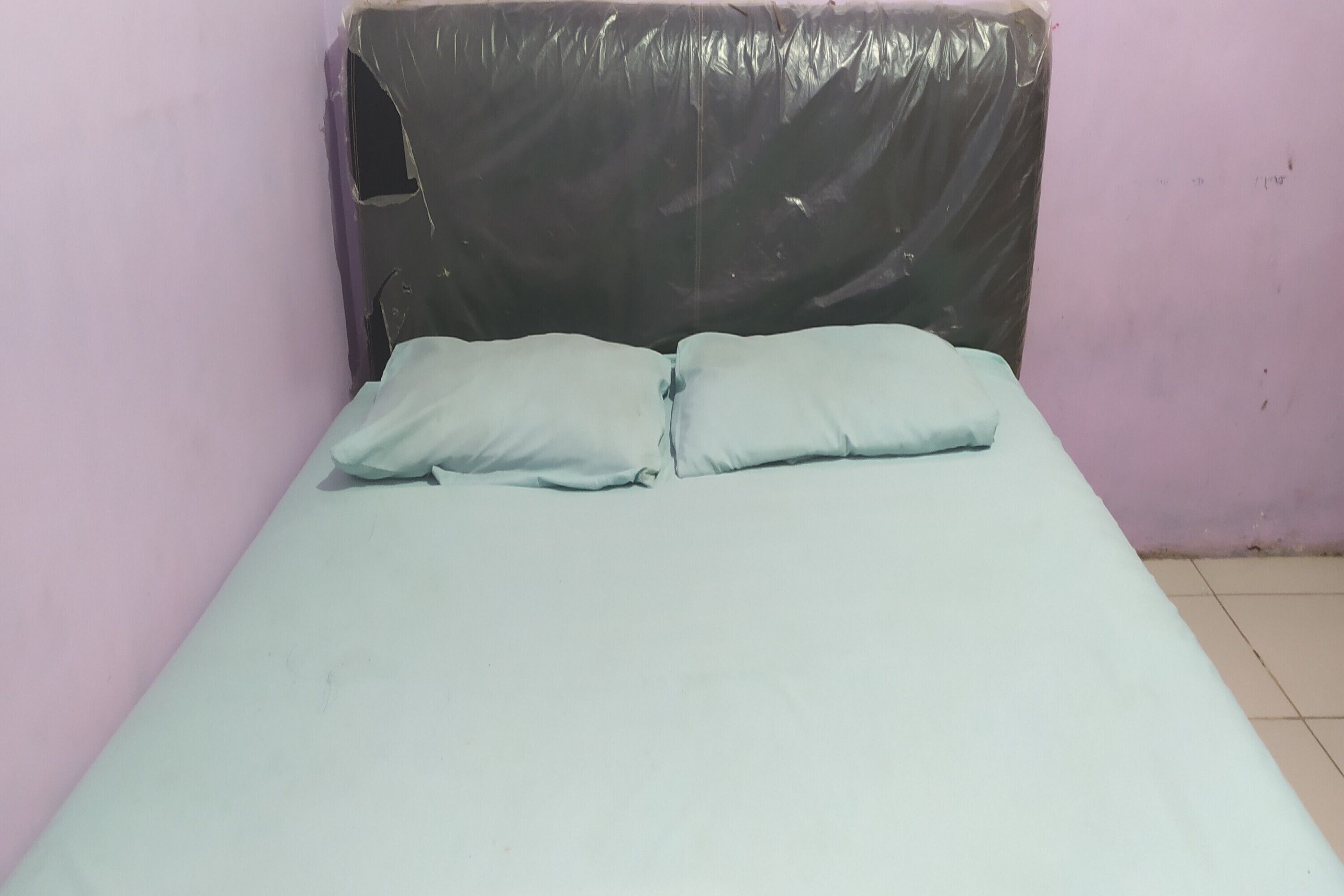 A bed with two pillows and a black plastic cover on the headboard.