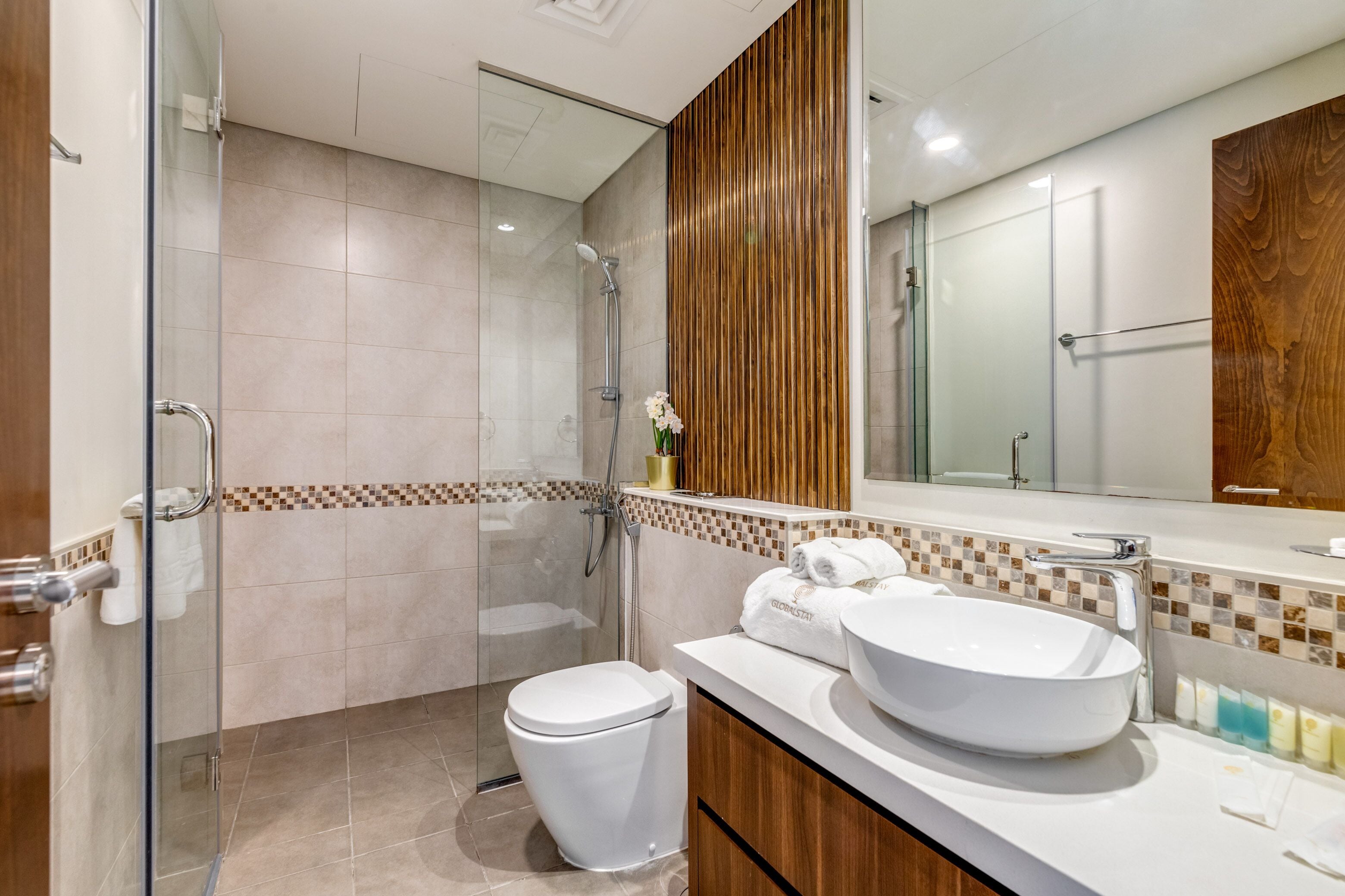 A modern bathroom with a glass shower enclosure, a white sink, and a wooden vanity.