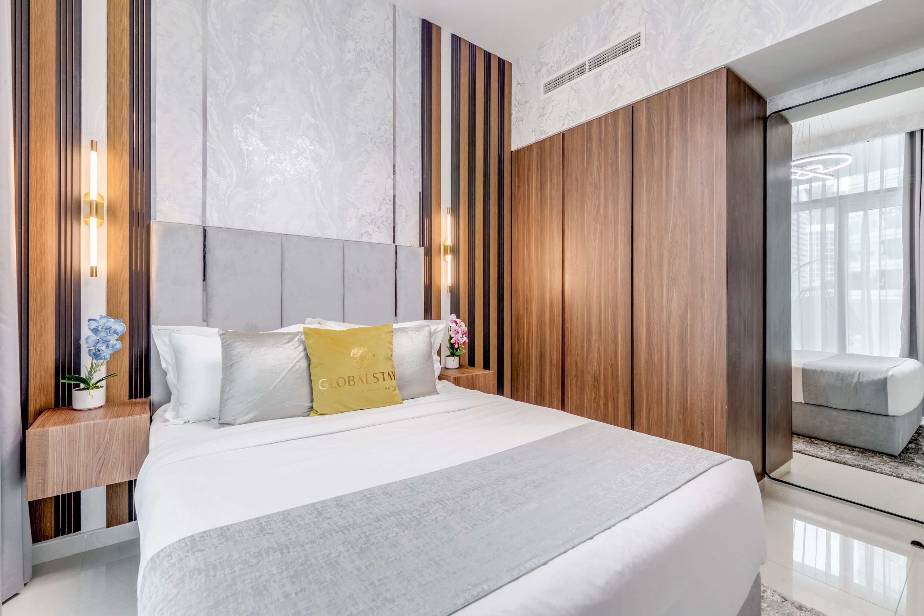 Una habitación de hotel moderna con una cama grande, paneles de madera, paredes de mármol y un espejo amplio.