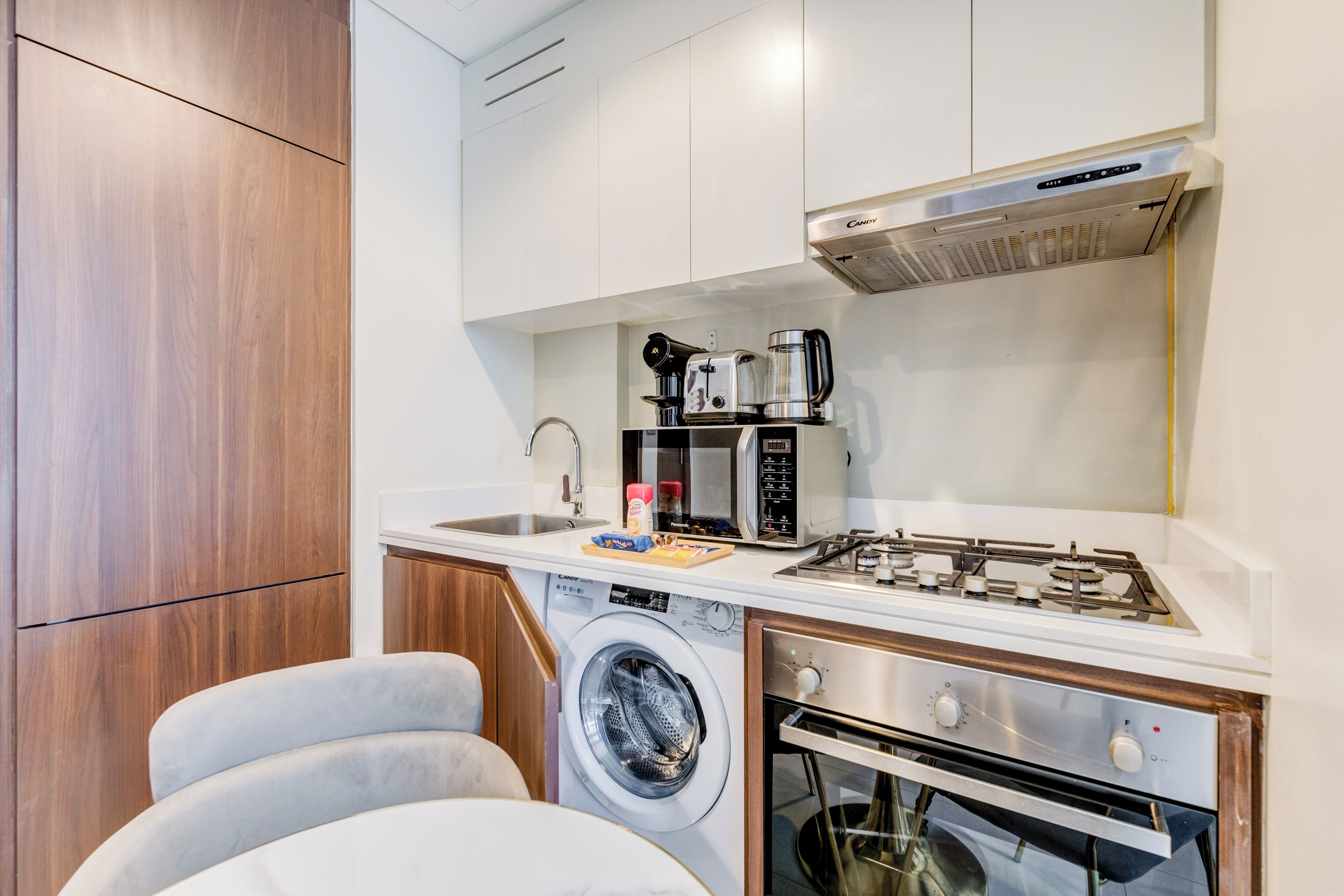 A compact kitchen with a washing machine, a microwave, a gas stove, and a built-in oven.