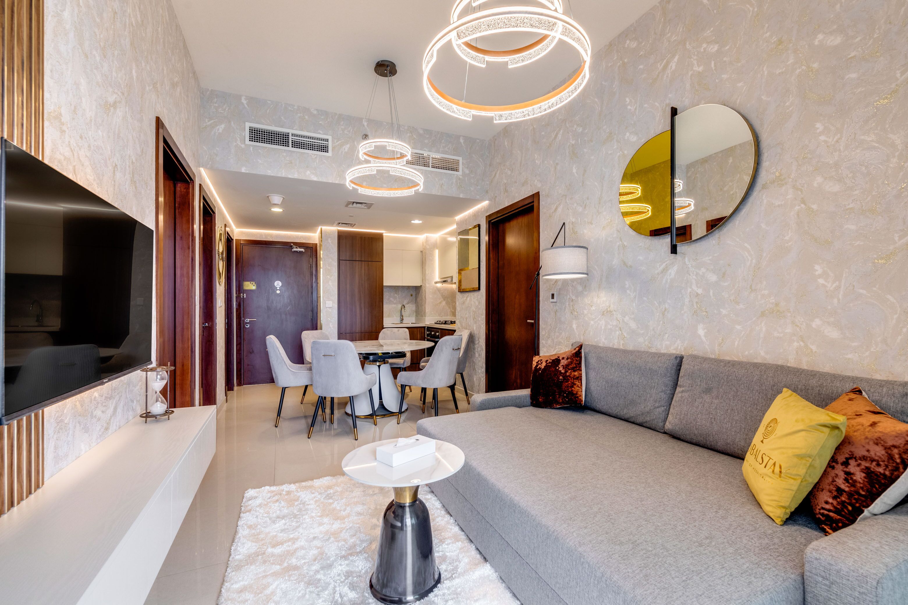 Una sala de estar moderna con un sofá gris, un espejo redondo y un comedor con mesa y sillas.