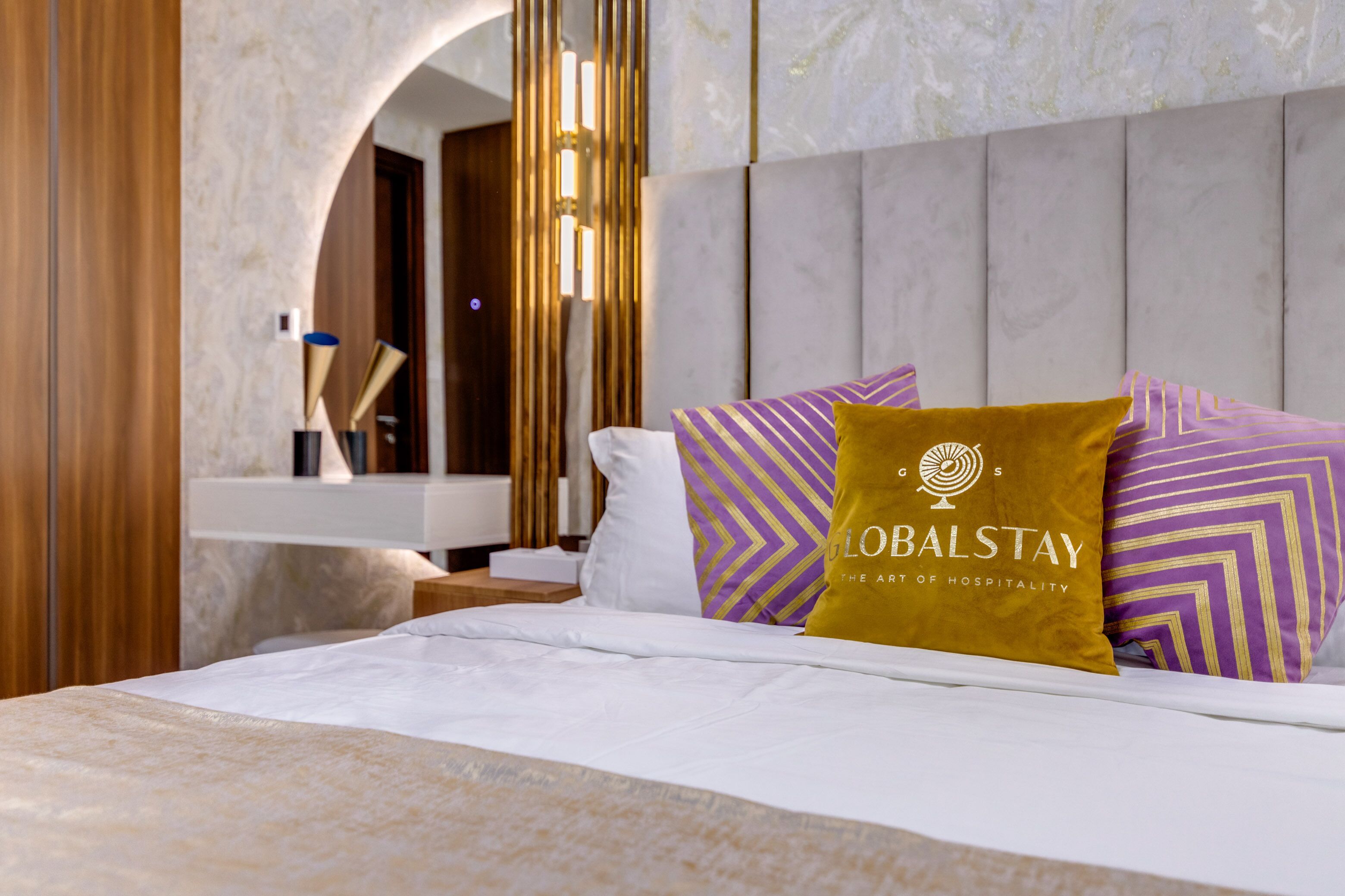 Habitación de hotel con cama, mesita de noche, espejo y lámpara de pared.