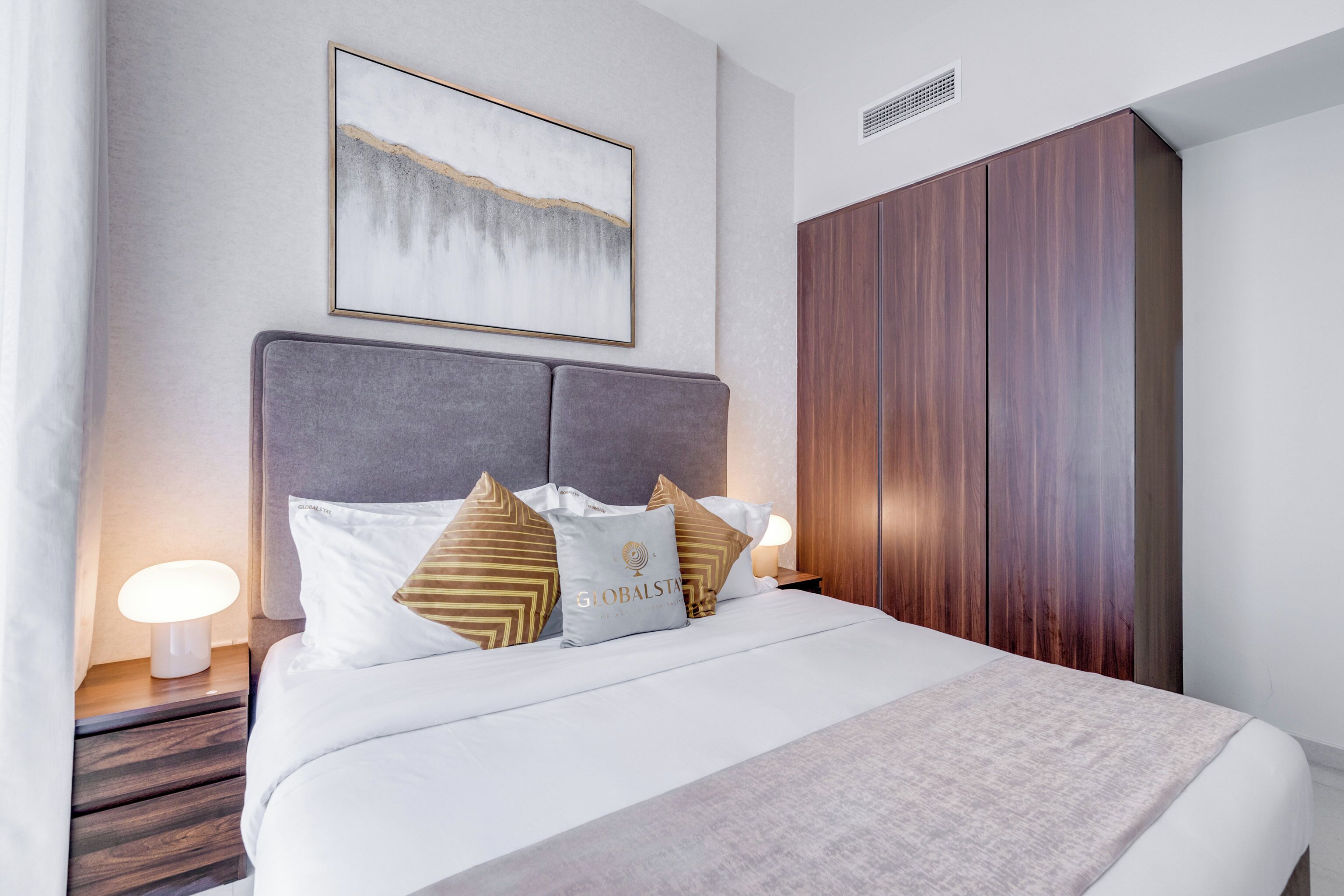 Une chambre d’hôtel moderne avec un grand lit, une tête de lit grise et une armoire en bois.