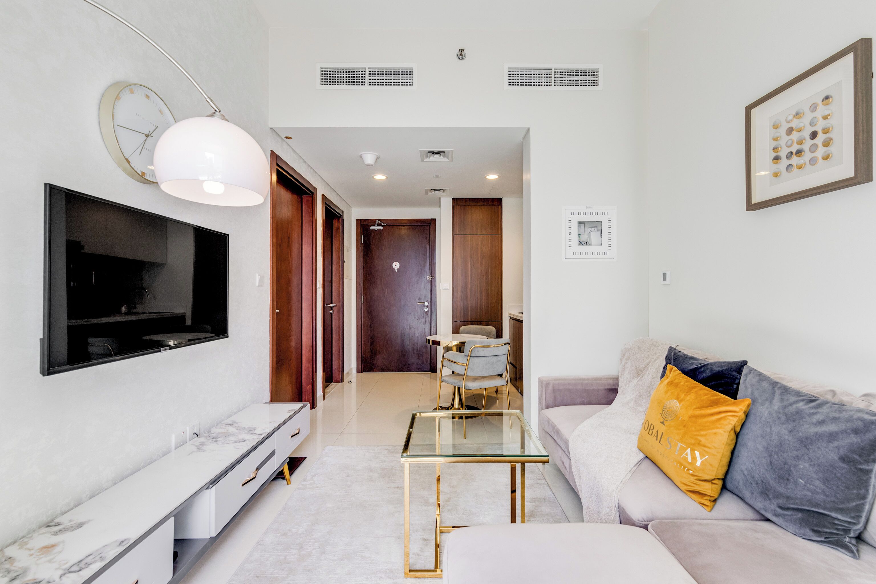 A modern living room with a flat-screen TV, a glass coffee table, a sofa with a cushion, and a framed artwork on the wall.
