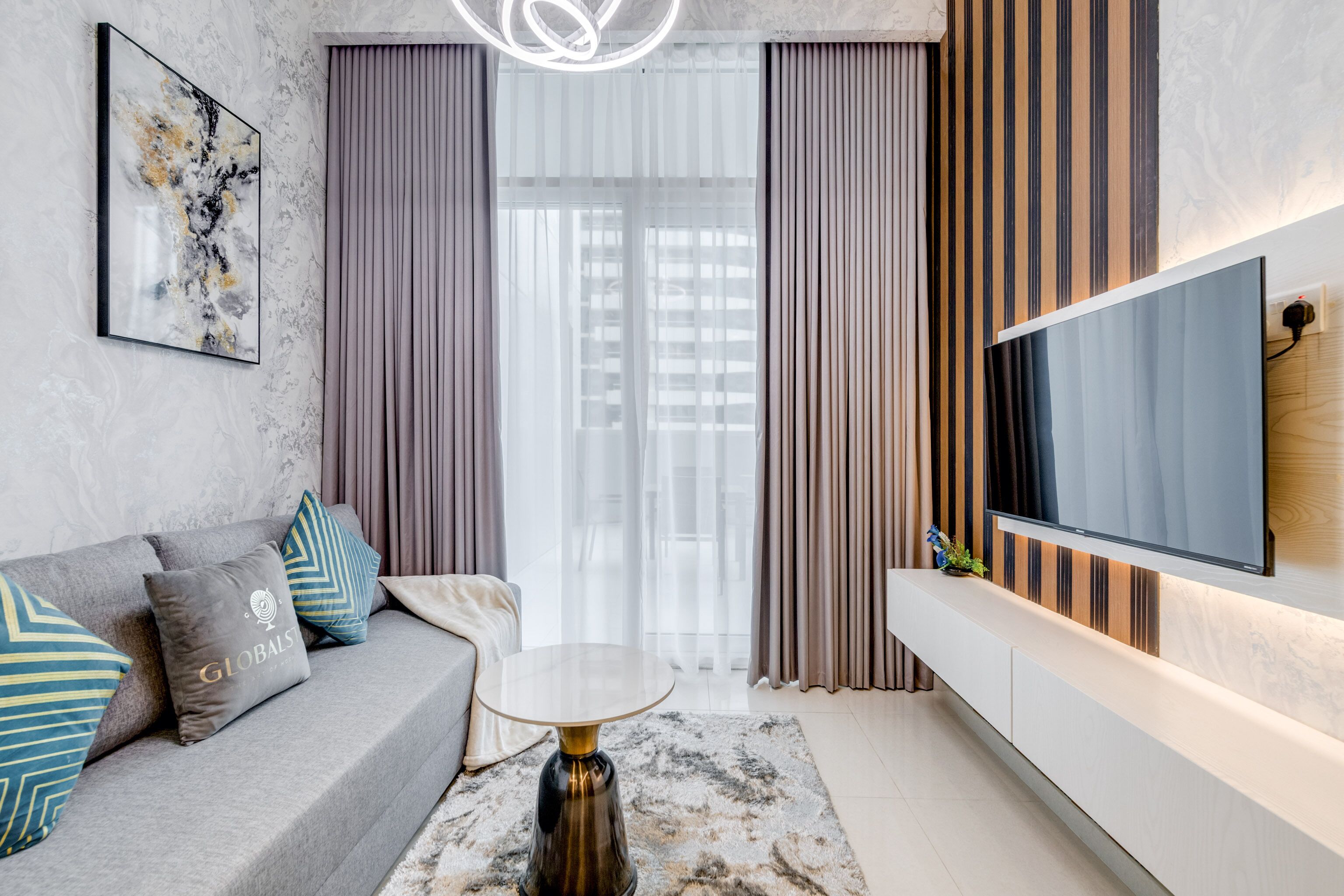 A modern living room with a grey sofa, a round coffee table, and a flat-screen TV mounted on the wall.