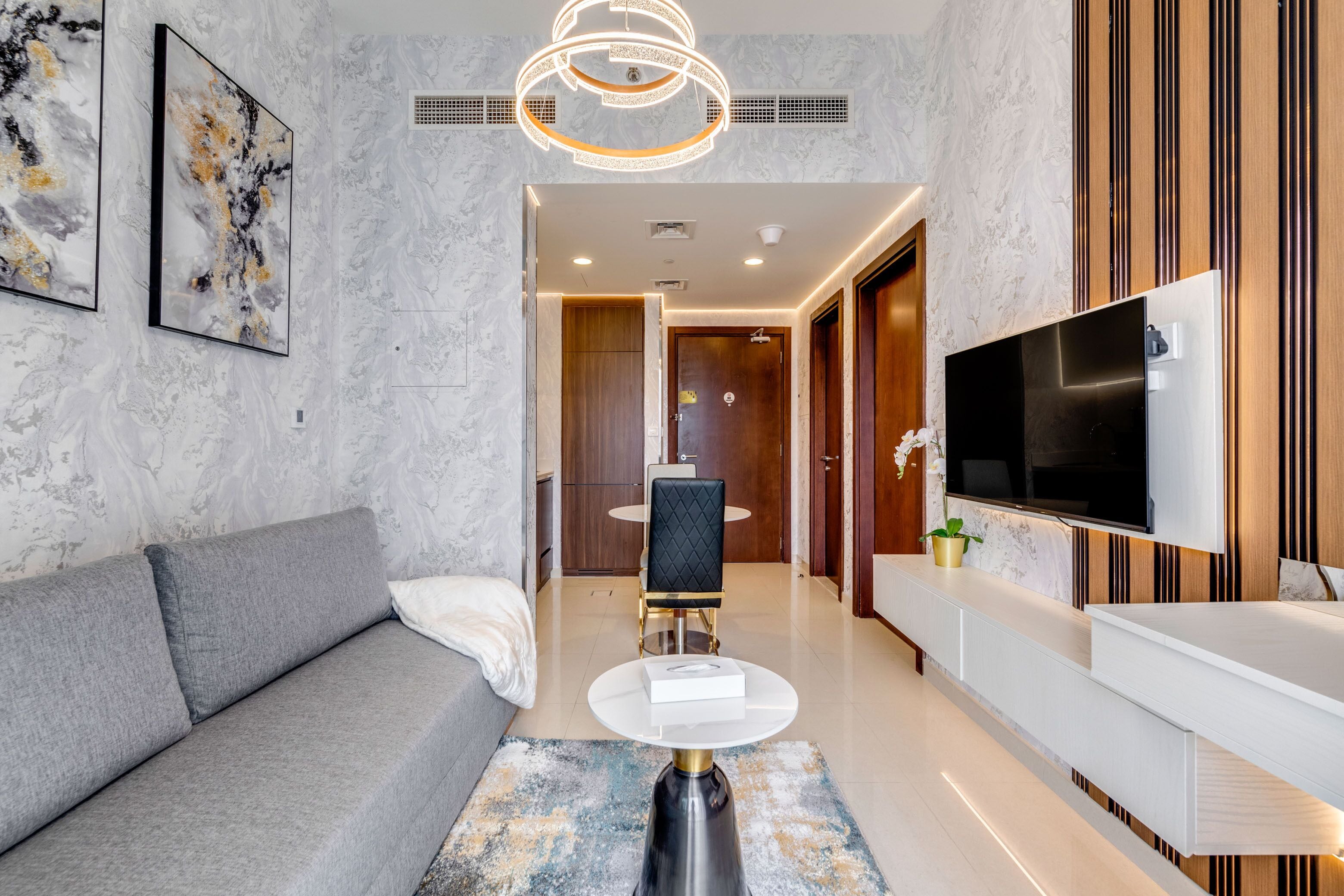 Un salon moderne avec un canapé gris, une table basse ronde et un téléviseur à écran plat fixé au mur.
