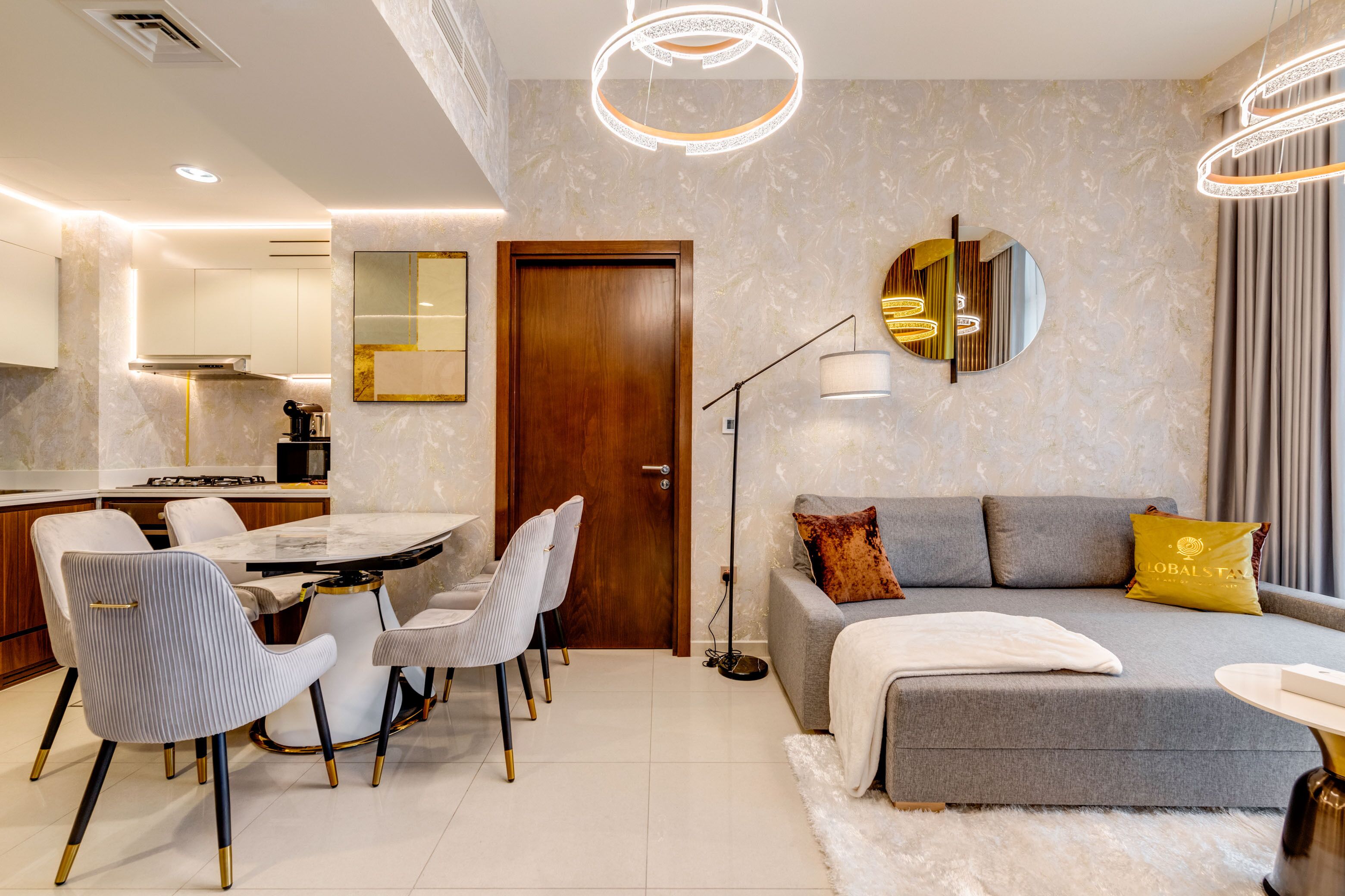 Ein modernes Wohnzimmer mit grauem Sofa, einem runden Couchtisch und einem Essbereich mit Marmortisch und gestreiften Stühlen.