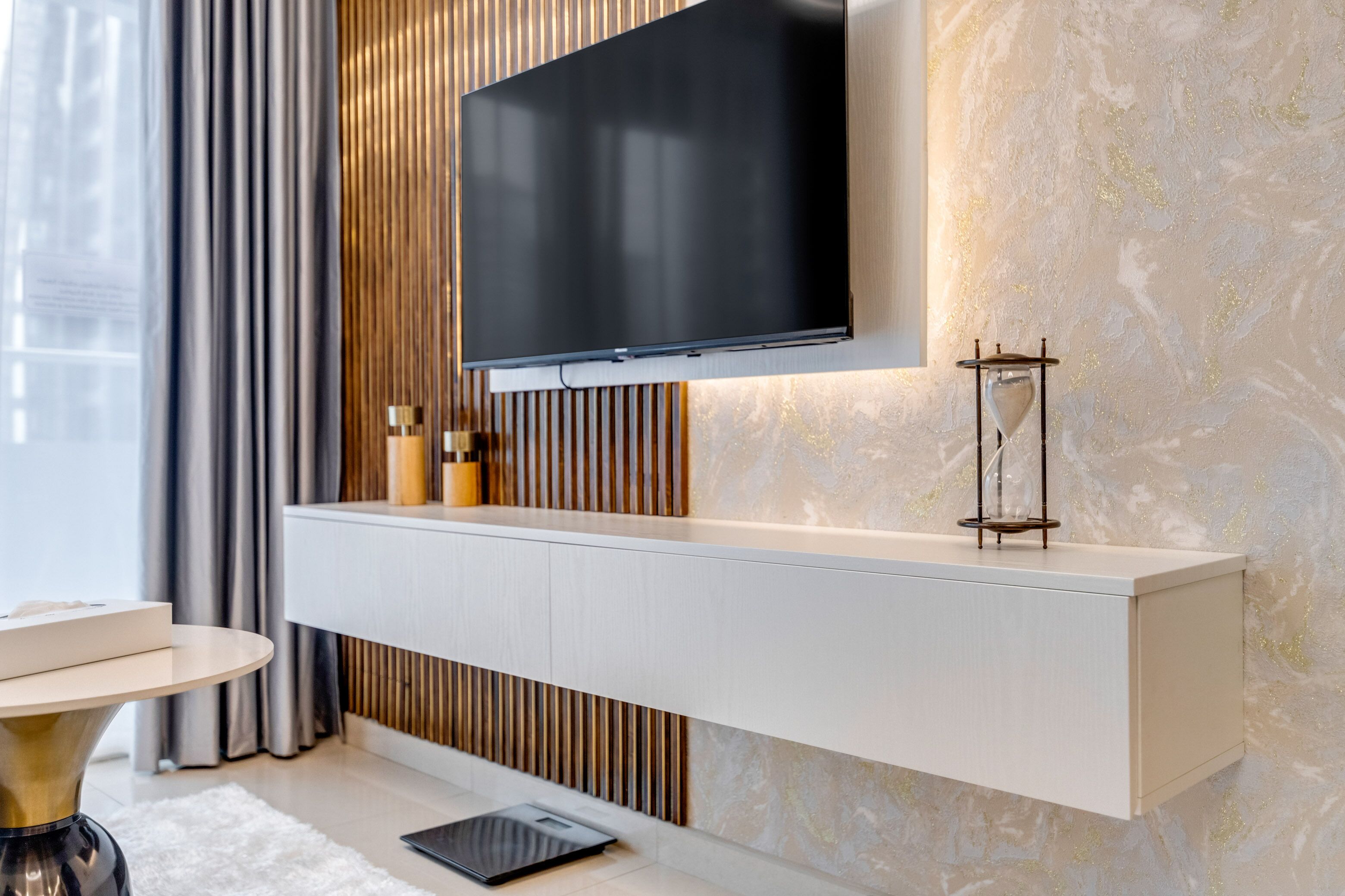 A modern living room with a flat-screen TV mounted on a wall, a white console table, and a glass coffee table.