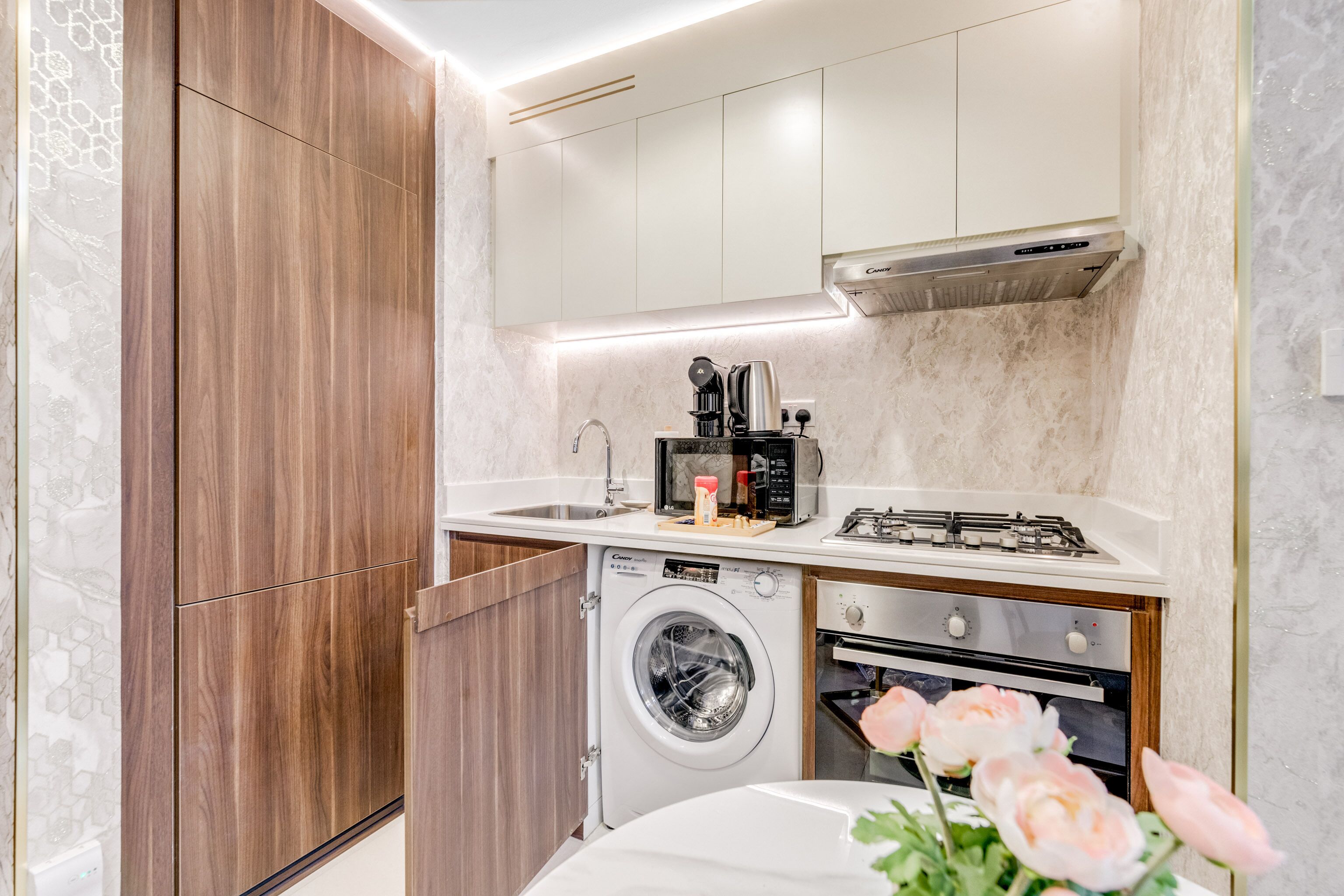 Cocina compacta con armarios de madera, lavadora integrada, microondas y cocina a gas.