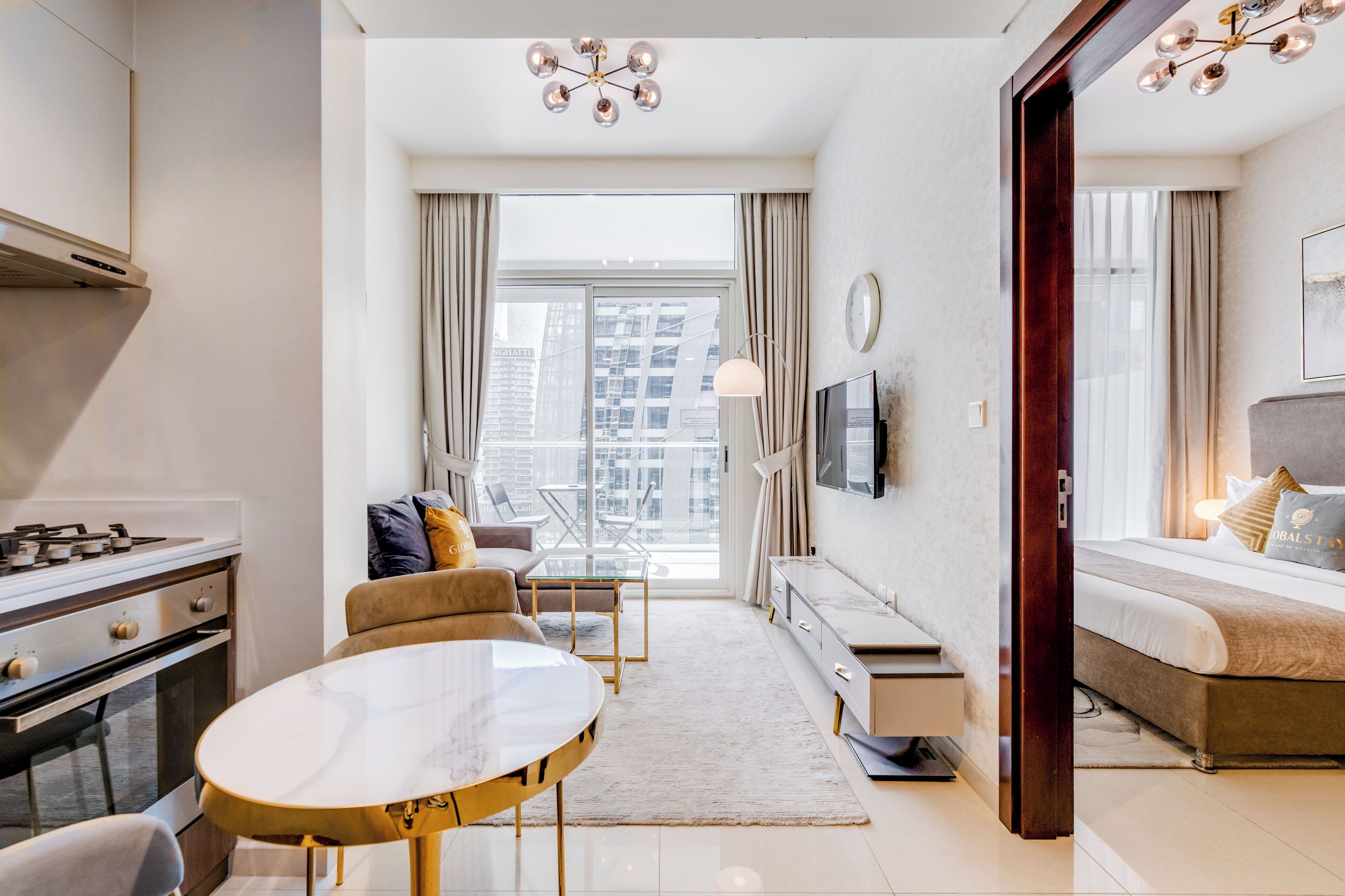 A modern hotel room with a dining area, a sofa, a TV, and a large window with a city view.