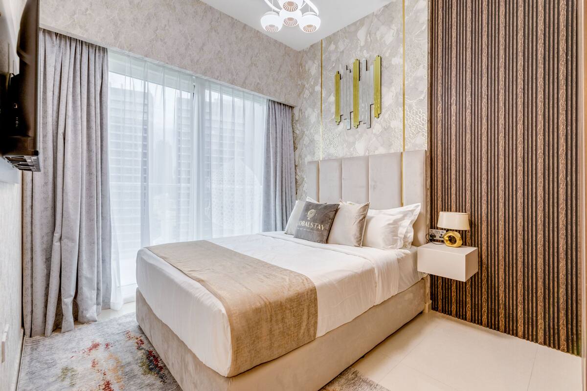 A modern bedroom with a large bed, a bedside table with a lamp, and a wall-mounted artwork.