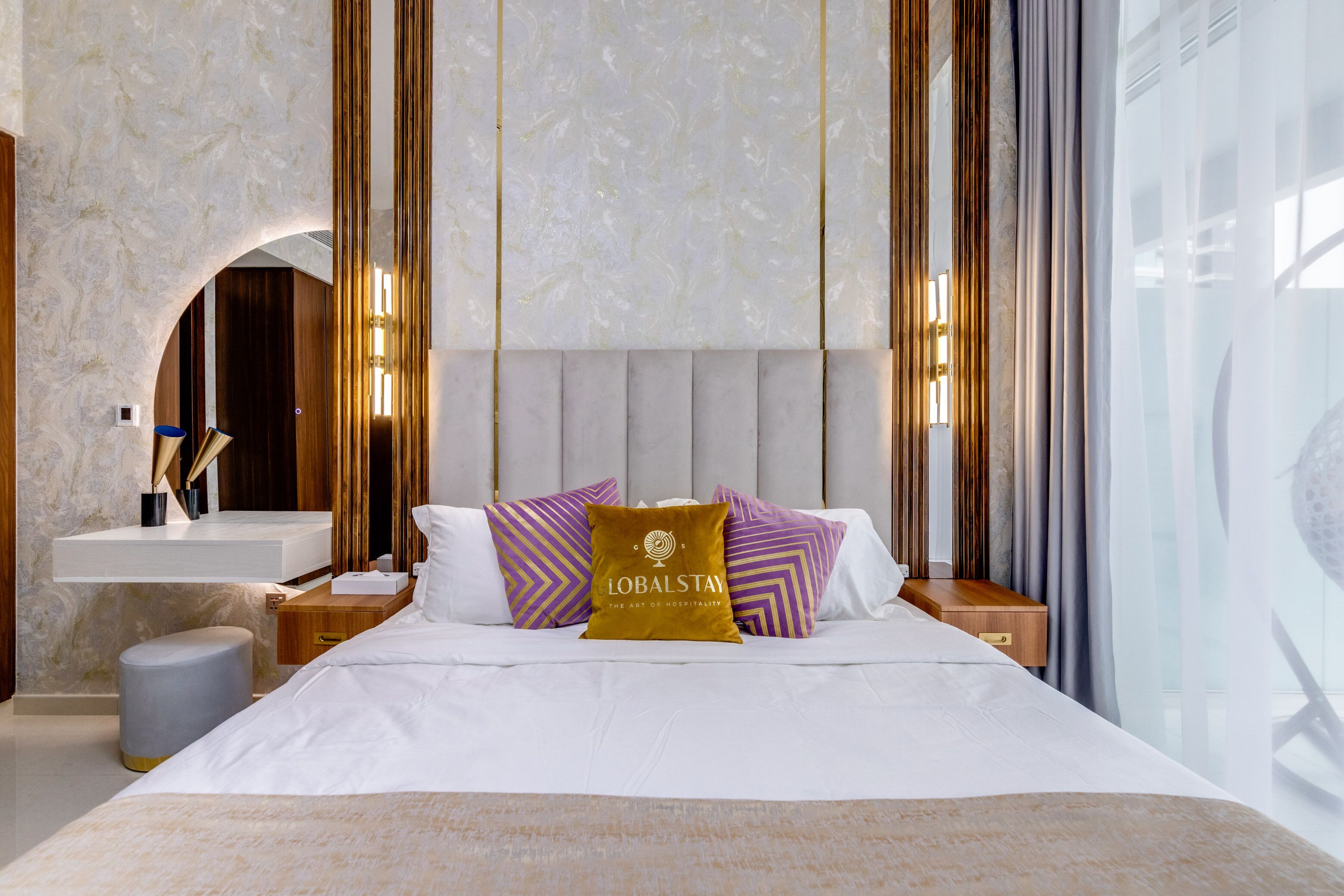 A modern hotel room with a large bed, a vanity with a mirror, and a view of the outdoors.