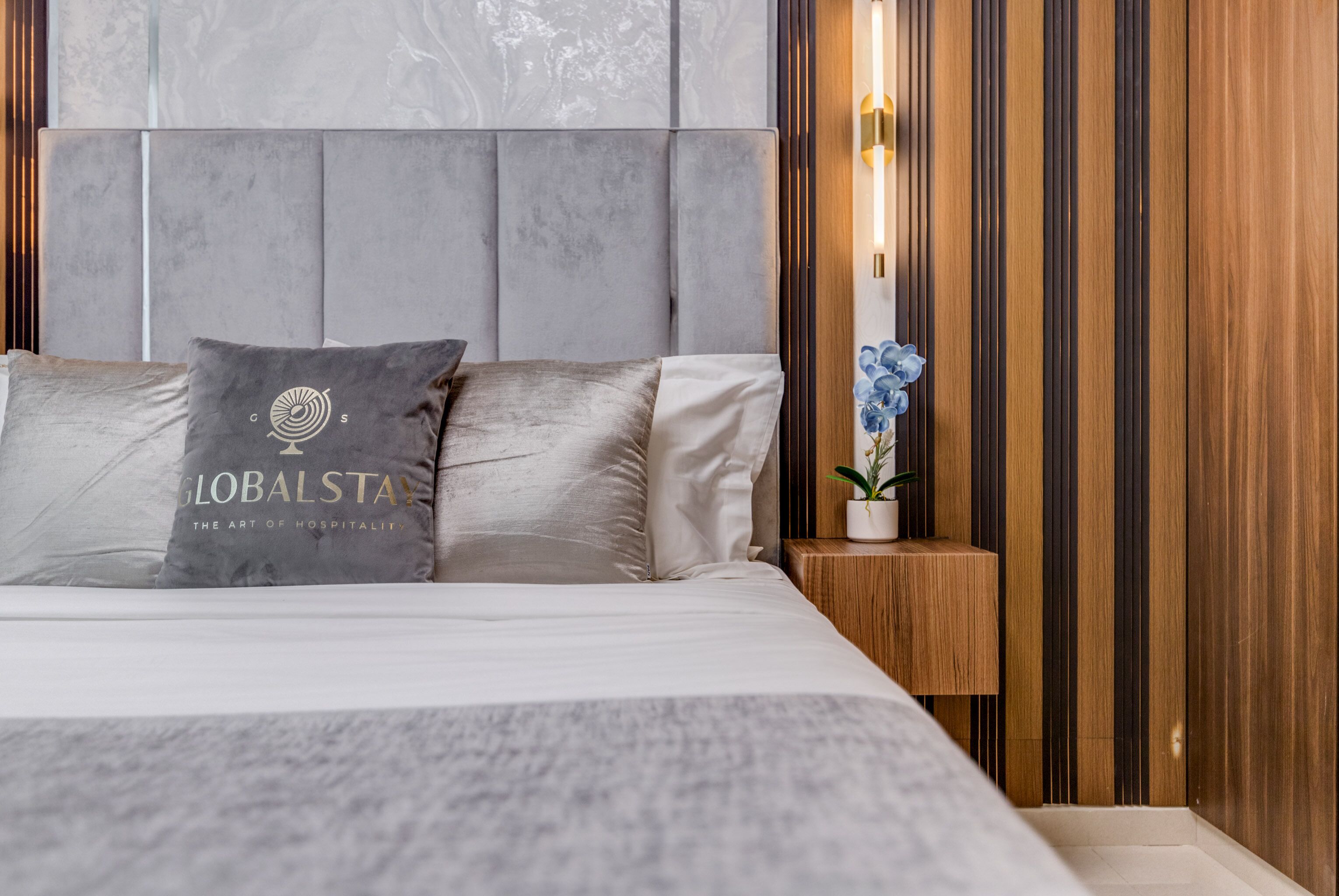 A modern hotel room with a large bed, a nightstand with a lamp, and a decorative plant.