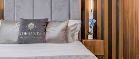 A modern hotel room with a large bed, a nightstand with a lamp, and a decorative plant.