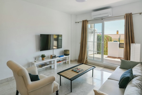 A modern living room with a flat-screen TV, a sofa, a coffee table, and a sliding glass door leading to an outdoor area.