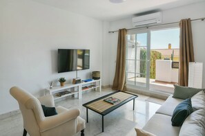 A modern living room with a flat-screen TV, a sofa, a coffee table, and a sliding glass door leading to an outdoor area.