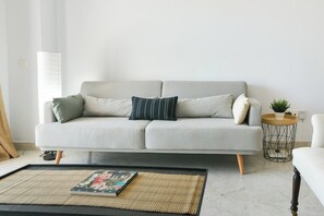 A modern living room with a grey sofa, a small round side table with a plant, and a black coffee table with a magazine.