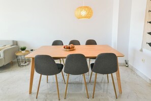 Un comedor con una mesa de madera, seis sillas grises, una lámpara colgante de fibras naturales y una mesita auxiliar con una planta.