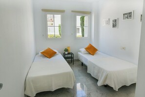 A room with two single beds, a small table with a lamp, and a window with a view of greenery.