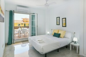 Un dormitorio con cama, mesita de noche, ventilador de techo y vistas a un área exterior con sillas a través de un ventanal.