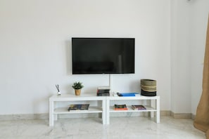 A modern living room with a flat-screen TV mounted on the wall, a white console table with books and decorative items, and a marble floor.
