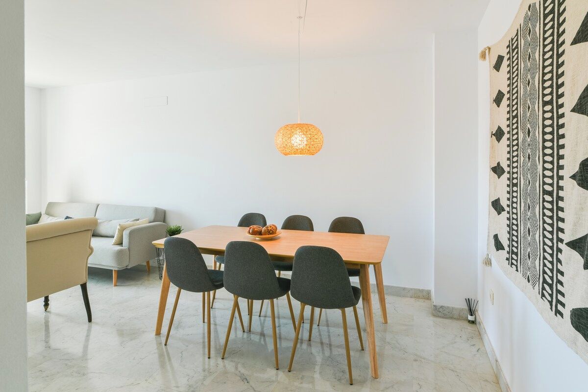 A dining area with a wooden table, six chairs, and a hanging light fixture.