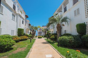 A pathway flanked by white buildings with balconies, palm trees, and well-maintained greenery.