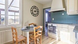 A kitchen with a round table, wooden chairs, a clock, and a view of the outside. - Family House in Montmartin-sur-Mer (Montmartin-sur-Mer)