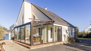 A modern house with a glass conservatory, a dining area, and a visible clock. - Family House in Montmartin-sur-Mer (Montmartin-sur-Mer)