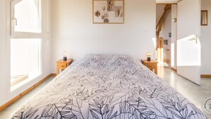 A bedroom with a bed, two bedside tables, a chandelier, a framed artwork on the wall, and a door leading to another room. - Family House in Montmartin-sur-Mer (Montmartin-sur-Mer)