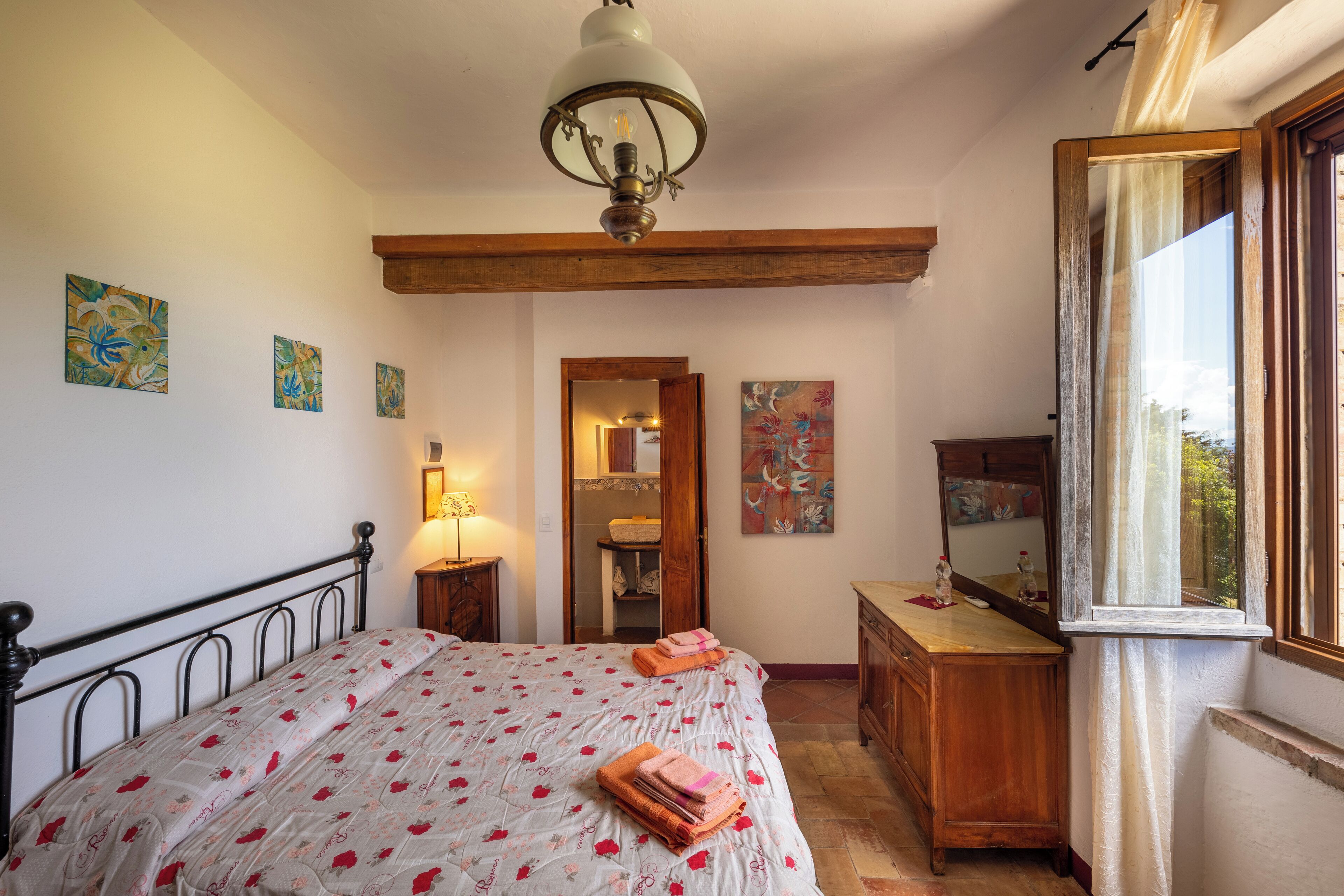 A bedroom with a bed, a wooden dresser, a mirror, and artwork on the walls.