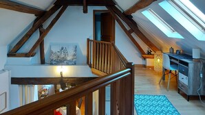 Un dormitorio tipo loft con techo inclinado, vigas de madera, tragaluces, una escalera, un comedor y vista del salón abajo.