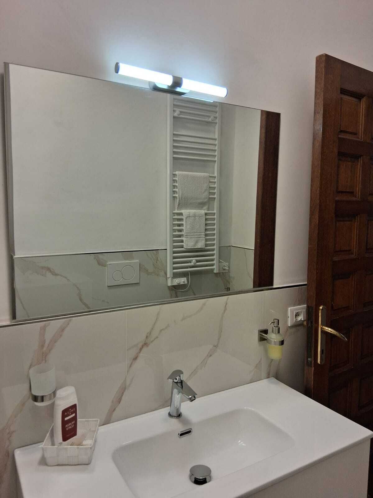 Une salle de bain avec un lavabo blanc, un miroir, un porte-serviettes et une porte en bois.