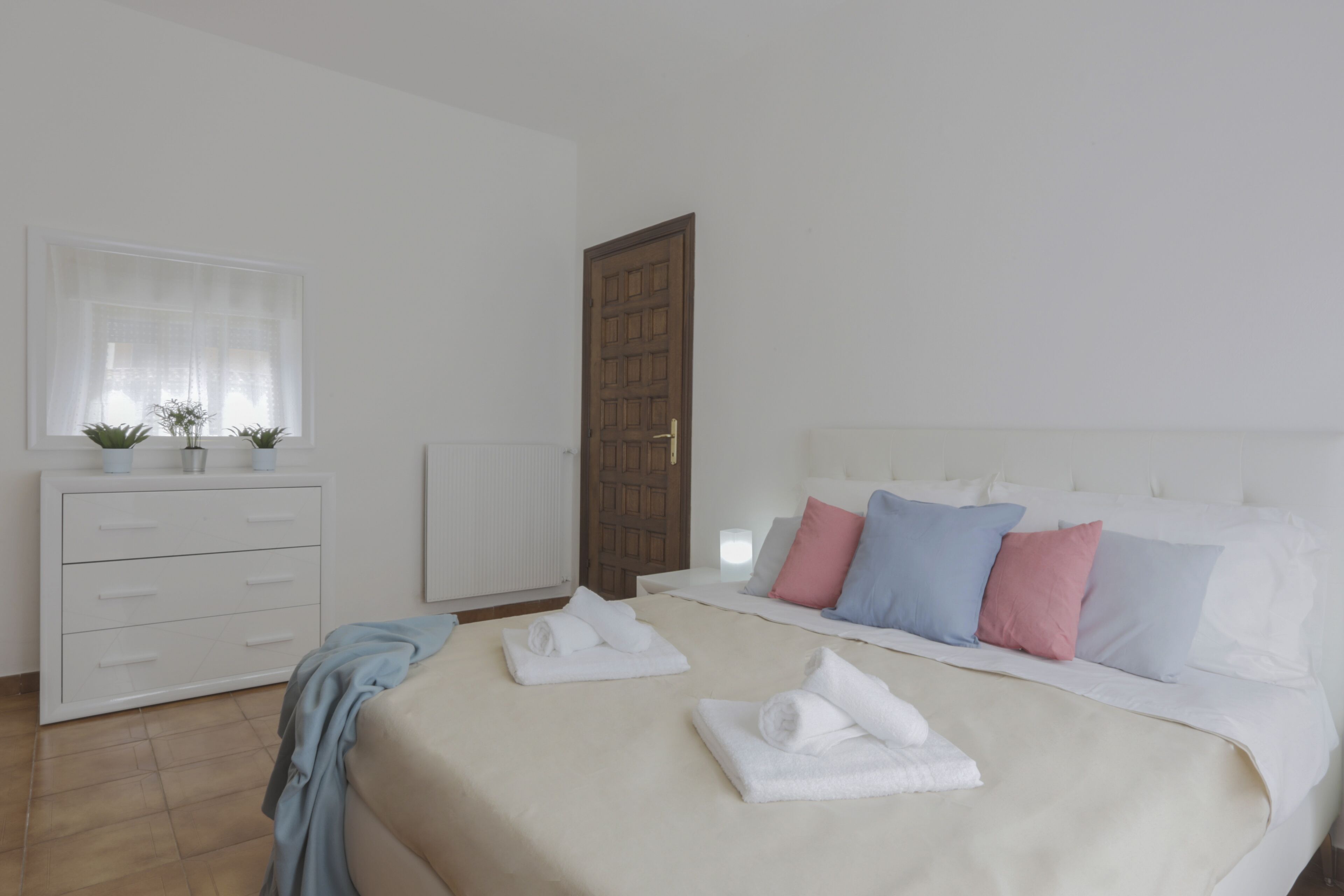 Un dormitorio con una cama grande, un aparador blanco y una ventana con cortinas de gasa.
