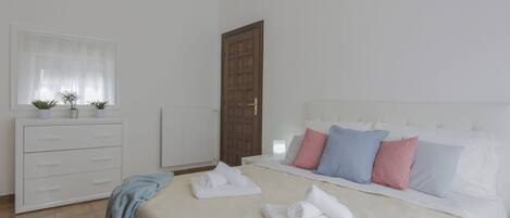 Un dormitorio con una cama grande, un aparador blanco y una ventana con cortinas de gasa.