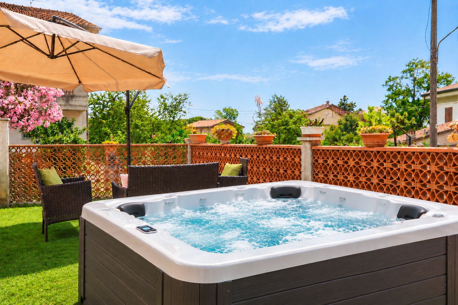 A hot tub in a backyard with a wooden fence, chairs, and a patio umbrella.